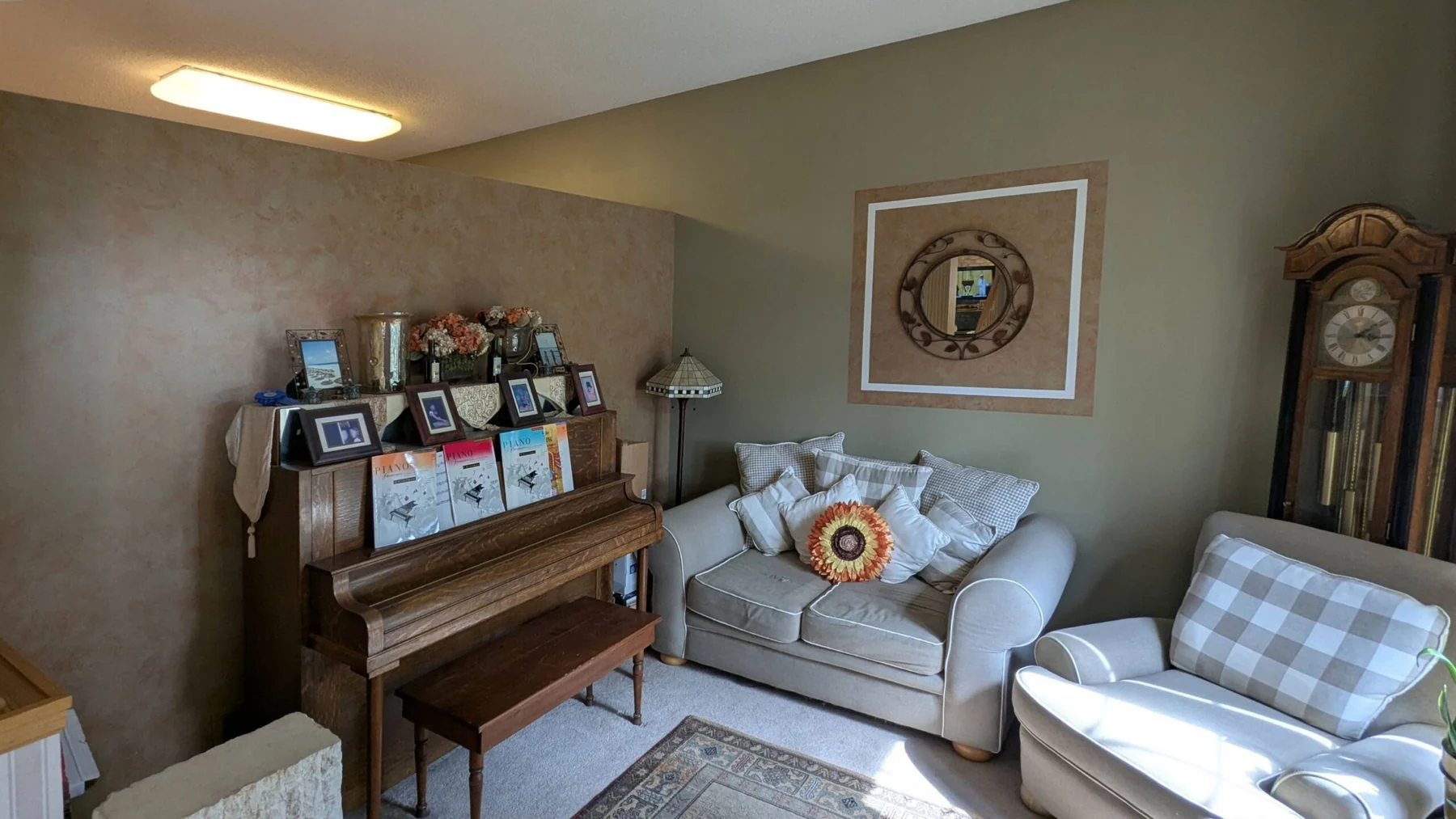 Living room with a wooden piano, a beige loveseat, and a grandfather clock in Woodbury MN